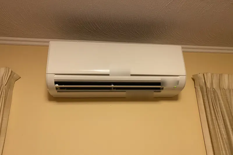 A white ductless indoor unit mounted high on a yellow wall between two curtains